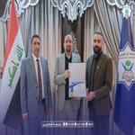 Four men in suits pose at an official signing event with flags in the background and one man displaying a signed document   جامعة الرافدين   مدير الموقع عمار محمود ابو الشعير