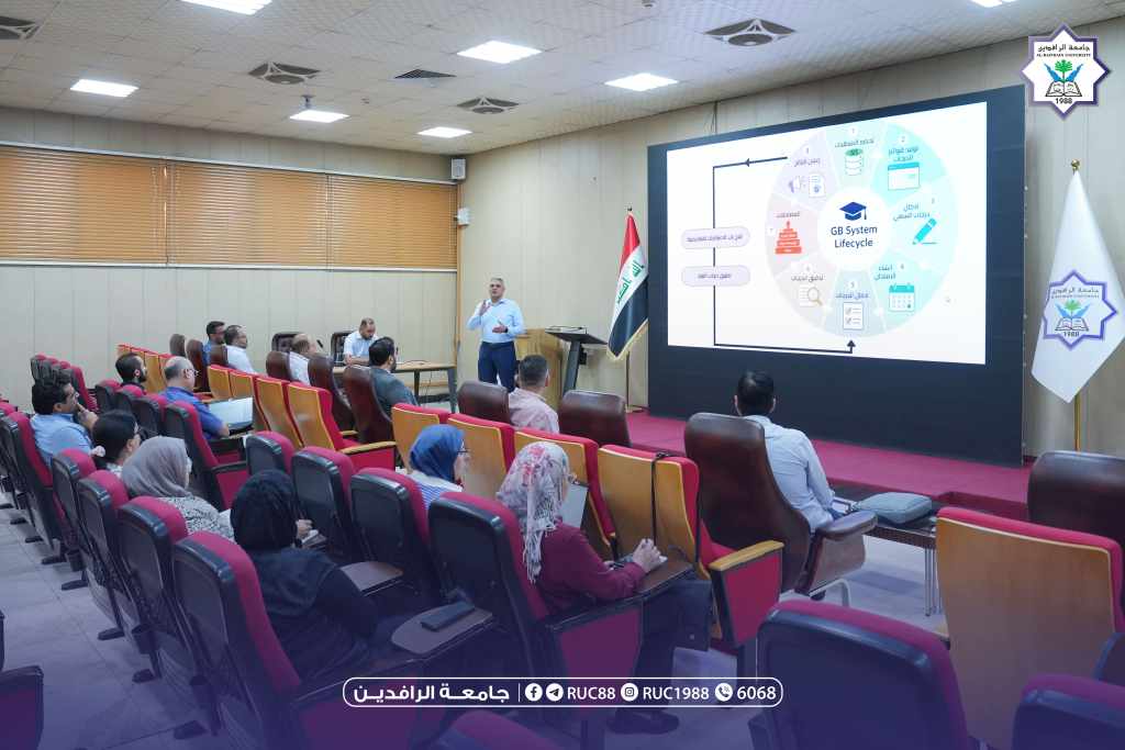 DSC00555 1 جامعة الرافدين 2026 Speaker presenting a slide deck to an audience in a university lecture hall with an Iraqi flag and institutional logos visible near the screen جامعة الرافدين مدير الموقع عمار محمود ابو الشعير