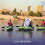 Three people riding green jet skis on calm water near a city shoreline with a large circular banner between two of them   جامعة الرافدين   مدير الموقع عمار محمود ابو الشعير   جامعة الرافدين   مدير الموقع عمار محمود ابو الشعير