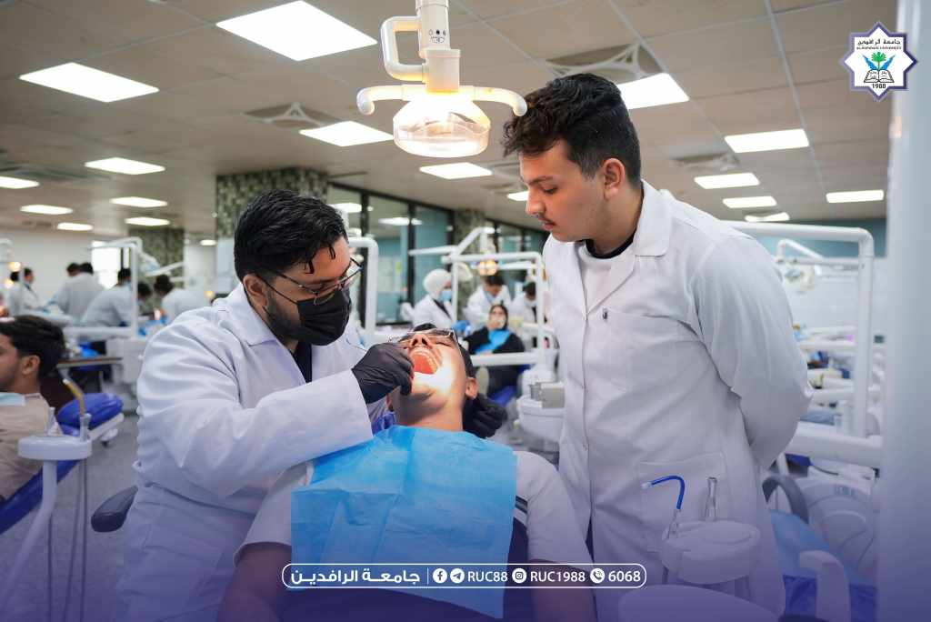 DSC09793 1 جامعة الرافدين 2026 Dentists in white coats treating a patient in a university dental clinic with overhead light and other students in the background logo in the corner جامعة الرافدين مدير الموقع عمار محمود ابو الشعير