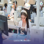 Woman in a white headband examines a small handheld device at a busy classroom workshop   جامعة الرافدين   مدير الموقع عمار محمود ابو الشعير   جامعة الرافدين   مدير الموقع عمار محمود ابو الشعير