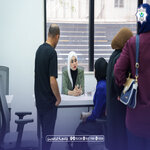 Reception area with a staff member assisting a client at a desk while others wait nearby in a modern office   جامعة الرافدين   مدير الموقع عمار محمود ابو الشعير   جامعة الرافدين   مدير الموقع عمار محمود ابو الشعير